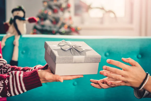 Mother giving christmas present to daughter while sitting on sofa at home