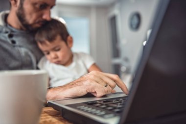 Baba evde dizüstü bilgisayarda çalışma office ve oğlunu kucağına holding