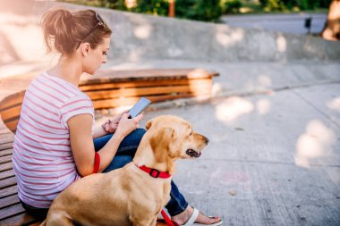 Parkta köpeğiyle oturan ve telefon kullanan bir kadın.