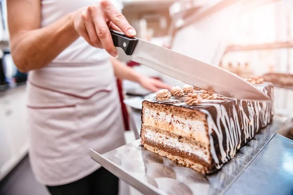 Pastry chef taking slice of chocolate cake with knife