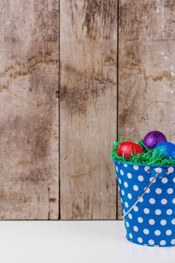 Mavi teneke kova ahşap duvar arka plan ile tabloda yeşil çim ile renkli Paskalya yumurtaları