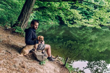Göl kenarında köpek ile ağaç günlük bankta oturmuş sakallı