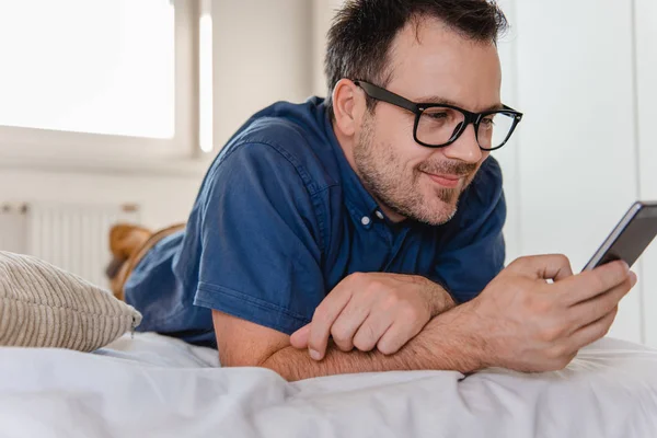 Man Glasses Blue Shirt Laying Bed Using Smart Phone — Stock Photo, Image