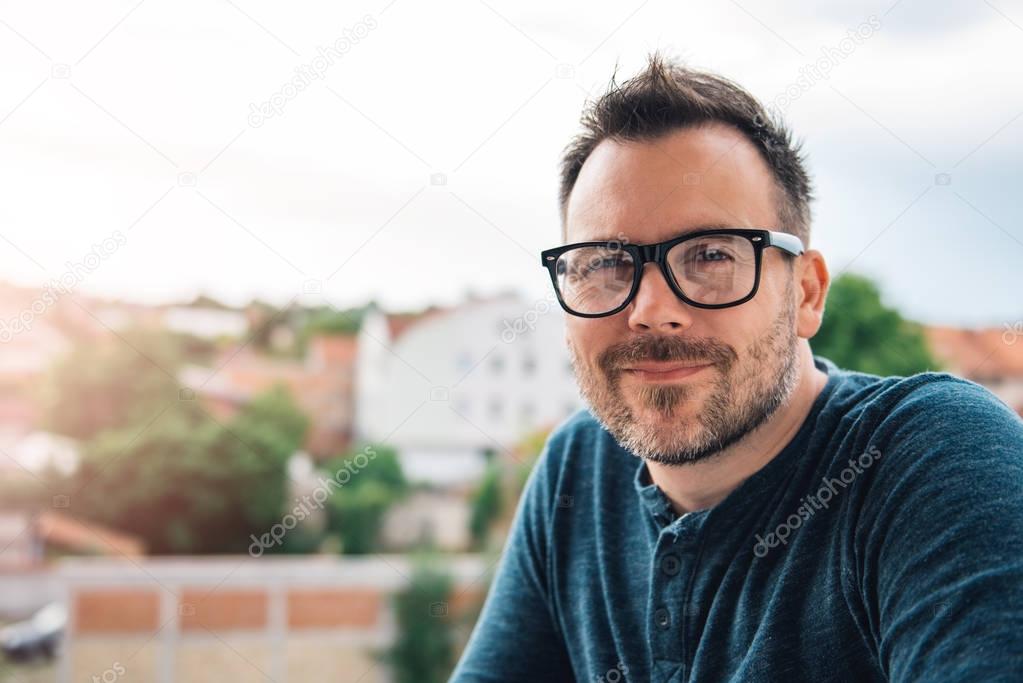 Man with glasses and beard waring blue shirt posing outdoor.