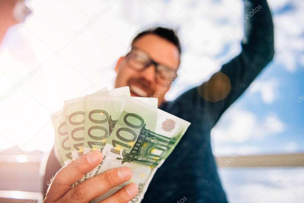 Man with glasses wearing blue shirt. and holding stack of money.