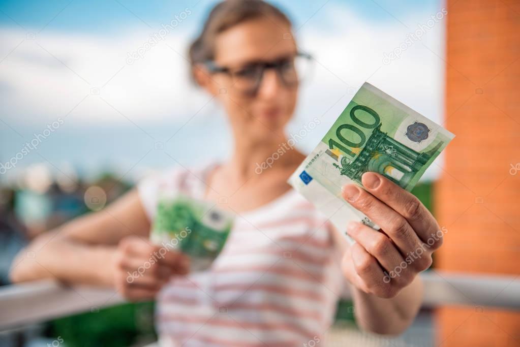 Woman with glasses holing money in her hands. She is holding European currency, 100 Euro bill.