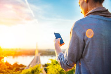 Günbatımı sırasında akıllı telefon kullanan kadın