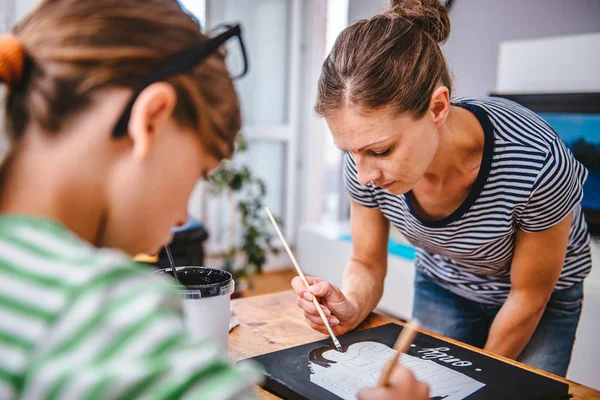 Art teacher helping a student with her painting during art class