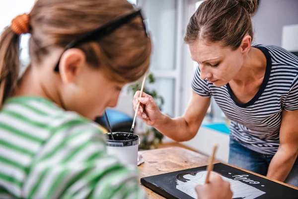 Art teacher helping a student with her painting during art class