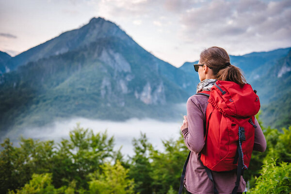 Woman with red backpack hiking on the mountain and looking at sunrise