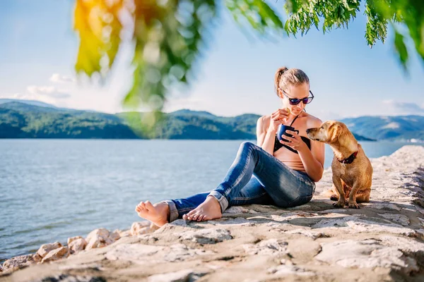 청바지 마시는 커피와 쿠키를 그녀의 노란색 강아지와 해변에서 비키니를 선글라스와 — 스톡 사진