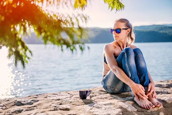 Kobieta Okulary Sobie Czarne Bikini Dżinsy Siedzi Kamień Dock Picia — Zdjęcie stockowe