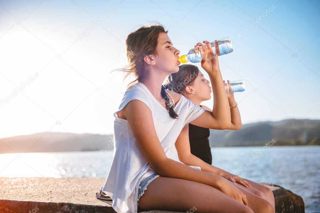 Two young girls sitting by the sea and drinking water from a PET bottle
