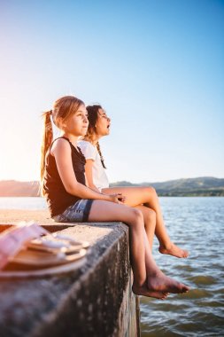 Birlikte deniz kenarında bir dock üzerindeki siting ve rahatlatıcı iki genç kız