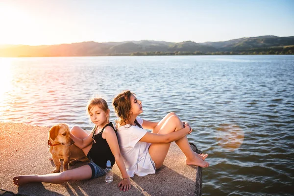 Dwie Dziewczyny Pies Siedzi Nad Wodą Zachód Słońca — Zdjęcie stockowe