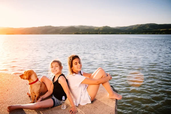 Dvě Dívky Pes Sedí Vody Užívat Západ Slunce — Stock fotografie