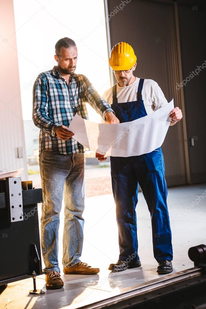 Construction workers checking checking blue print in big industrial hall