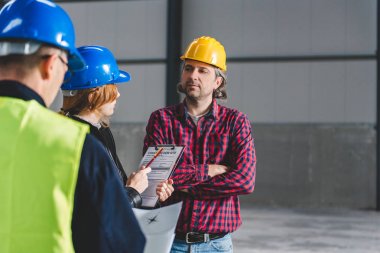 Denetim raporu büyük endüstriyel salonda yapma ve inşaat işçileri ile konuşurken sitesine Müfettiş