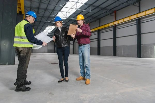 Site Inspector making inspection report in big industrial hall and talking with Construction workers