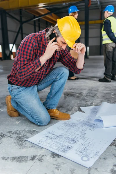 Bauarbeiter Schutzhelm Liest Baupläne Und Telefoniert Mit Dem Smartphone — Stockfoto