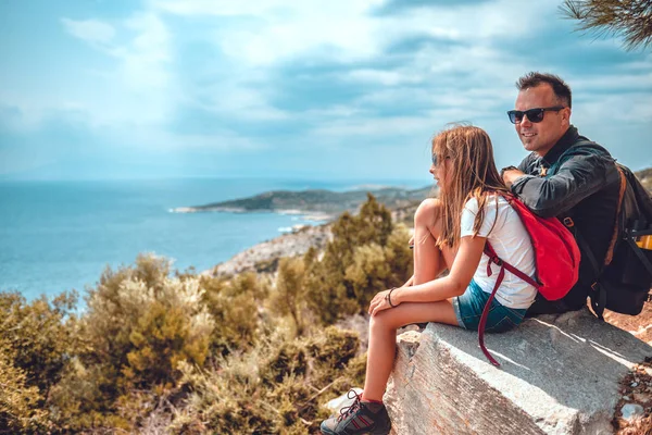 Apa és lánya a szikla szélén ülnek a tenger partján. — Stock Fotó