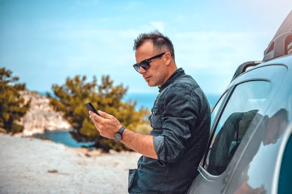 El hombre se apoya en el coche usando el teléfono inteligente —  Fotos de Stock