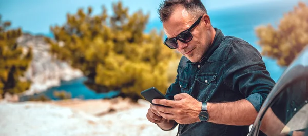 El hombre se apoya en el coche usando el teléfono inteligente Imagen De Stock