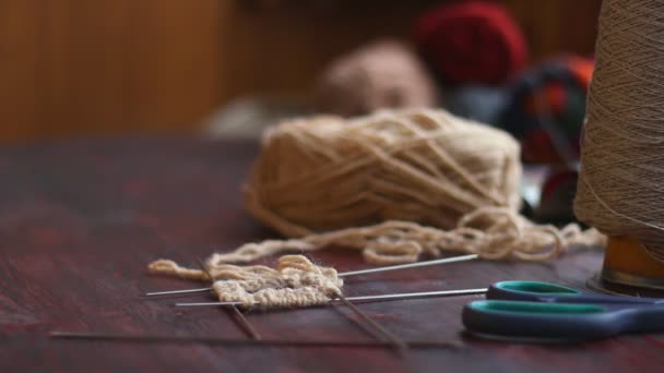 Close-up van handen van een jonge vrouw op een hout tabel breit een haarband met crème garen — Stockvideo