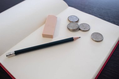 Tahta masada yeşil kalem, silgi ve Kolombiya paraları olan boş kırmızı defter.