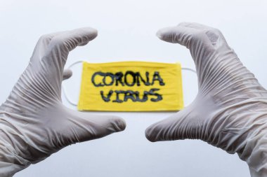 Beyaz Esterilize eldivenlere yakın. Siyah Coronavirus yazıtlı, siyah yüzlü sarı maskenin üstünde kızgın bir el ifadesi yapıyor. Covid 2019