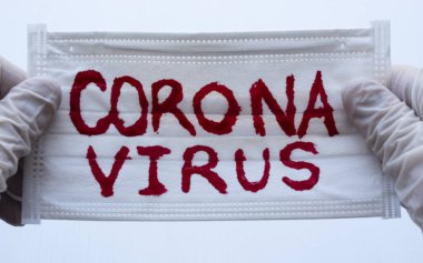Beyaz Yüz Maskesi 'ne kırmızı Coronavirus yazısıyla ve iki eli beyaz eldiven ya da onları tutan Esterilize kürelerle kapatılmış. Covid 2019