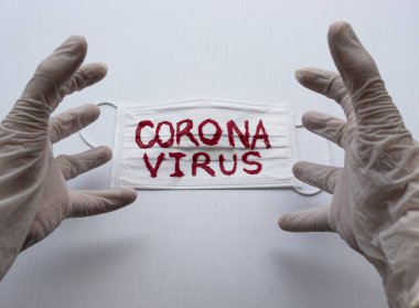 Beyaz Esterilize eldivenlere yakın beyaz yüz maskesinin üzerinde beyaz siyah zeminli kırmızı Coronavirus yazısıyla öfkeli bir el ifadesi yapıyor. Covid 2019