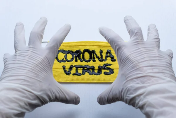 白い背景の黒いコロナウイルスの碑文と黄色の顔のマスクの上に怒りの手の式を作る白い滅菌手袋まで閉じられます Covid 2019 — ストック写真