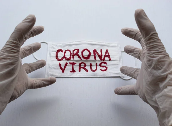 Beyaz Esterilize eldivenlere yakın beyaz yüz maskesinin üzerinde beyaz siyah zeminli kırmızı Coronavirus yazısıyla öfkeli bir el ifadesi yapıyor. Covid 2019