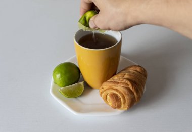 Geleneksel sıcak içeceği olan sarı kupa, limon ekleyen bir kişi, bir ekmek ve beyaz arka plan. 