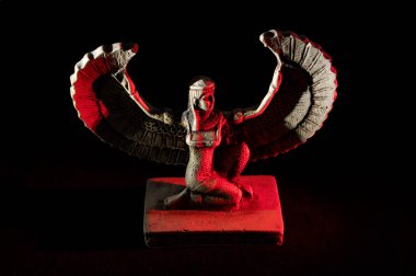 Isis 'e yakın. Eski kanatlı dişi Mısırlı tanrı figürü. Siyah arka planda beyaz ve kırmızı ışıklarla aydınlatılmış.