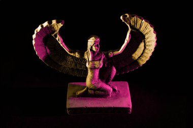 Isis 'e yakın. Eski kanatlı dişi Mısırlı tanrı figürü. Siyah arka planda sarı ve pembe ışıklarla aydınlatılmış.