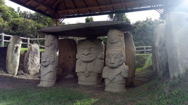 İki tarafı da Kolombiya San Agustin arkeoloji parkında iki savaşçıyla birlikte bir insan ocağı tutan bir rahip ya da şamanla birlikte antik bir dolmen. Antik kolomb öncesi kültür. 