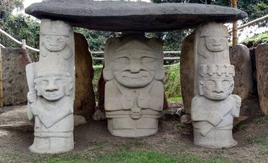 İki tarafı da Kolombiya San Agustin arkeoloji parkında iki savaşçıyla birlikte bir insan ocağı tutan bir rahip ya da şamanla birlikte antik bir dolmen. Antik kolomb öncesi kültür. 