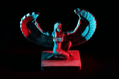 Closeup to a Isis. female old winged egyptian god mini figurine iluminated with red and blue lights over black background clipart