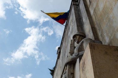 İki Taş Asker, Cementerio Central 'daki askeri mozoleyi koruyor. Arka planda dalgalanan Kolombiya bayrağı
