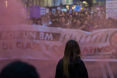 Bir kadın, Uluslararası Kadınlar Günü 'nde 8 M yürüyüşü sırasında arka planda kırmızı işaret fişeği olan bir kadın kalabalığını haklarını iddia ederek izliyor.