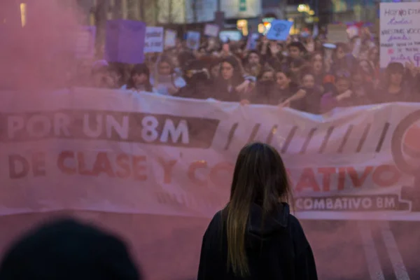 Bir kadın, Uluslararası Kadınlar Günü 'nde 8 M yürüyüşü sırasında arka planda kırmızı işaret fişeği olan bir kadın kalabalığını haklarını iddia ederek izliyor.