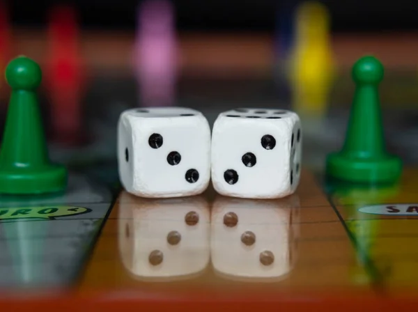 Macro photograhpy to an Old white dices with double three pair and color pawns over a board game