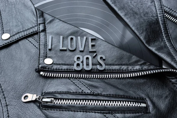 Closeup to a I love 80s lettering art over a black leather biker jacket with LP vinyl disc. Music lover concept, retro photography.