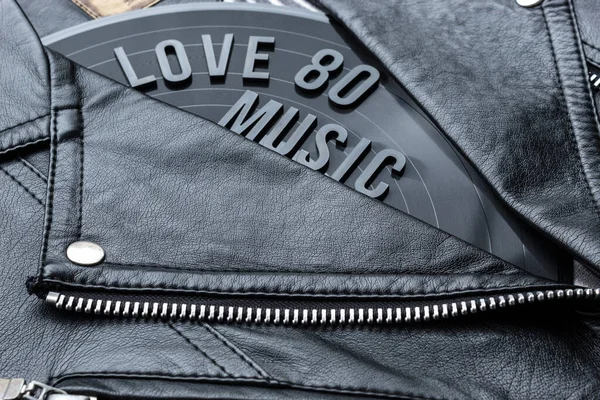 Closeup to a love 80 music lettering art over a black leather biker jacket with LP vinyl disc. Music lover concept, retro photography.