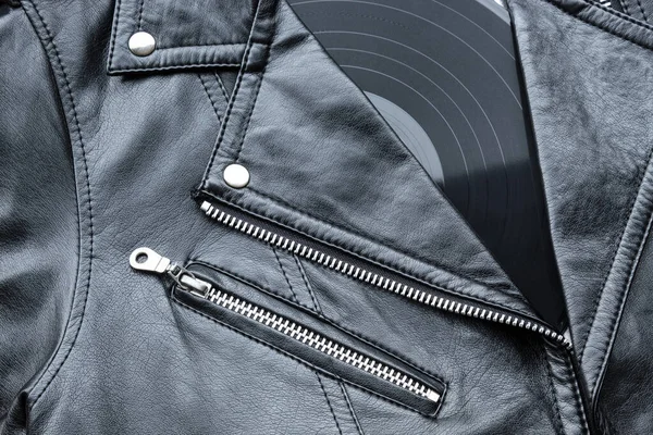 Closeup to a black leather biker jacket with LP vinyl disc. Music lover concept, retro photography.