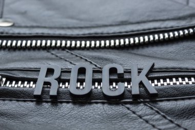 Siyah motosikletli deri ceketin üzerine siyah harf yazan bir rockçı. Rock müzik severler ve moda tarzı