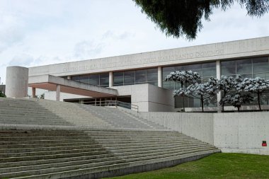 Julio Mario Santo Domingo Halk Kütüphanesi 'nin geometrik deseni yeşil çimen, ağaç ve doğa mimarisi olan beyaz merdivenleri. modern yapı cephesi
