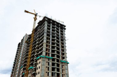 Yüksek sarı vinçli ve arka planda bulutlu bir binanın inşaatı